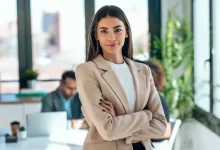 Mladá krásná žena stojí vs překříženýma rukama v byznysovém kostýmu v kanceláři