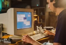Mladý muž sedí za starou retro počítačovou sestavou a pracuje na ní