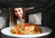 Mladá krásná rozesmátá žena vkládá jídlo k ohřevu do mikrovlnky