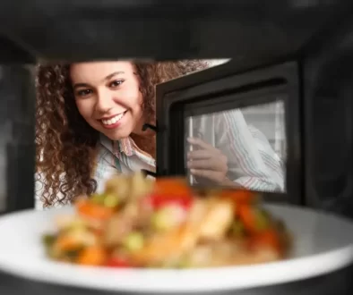 Mladá krásná rozesmátá žena vkládá jídlo k ohřevu do mikrovlnky