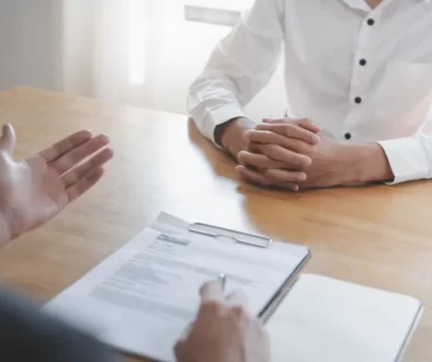 Detailní záběr na pohovor, kde zaměstnavatel probírá životopis uchazeče u pracovního stolu.