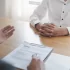 Detailní záběr na pohovor, kde zaměstnavatel probírá životopis uchazeče u pracovního stolu.