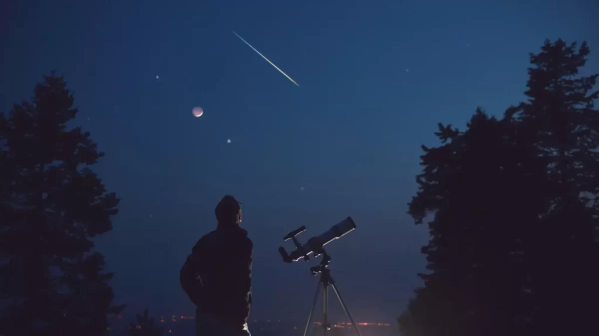 Muž s teleskopem pozorující večerní oblohu