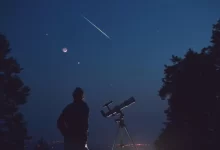 Muž s teleskopem pozorující večerní oblohu