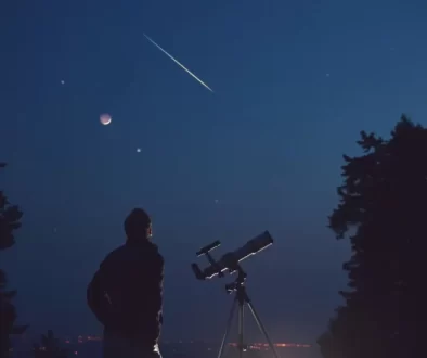 Muž s teleskopem pozorující večerní oblohu