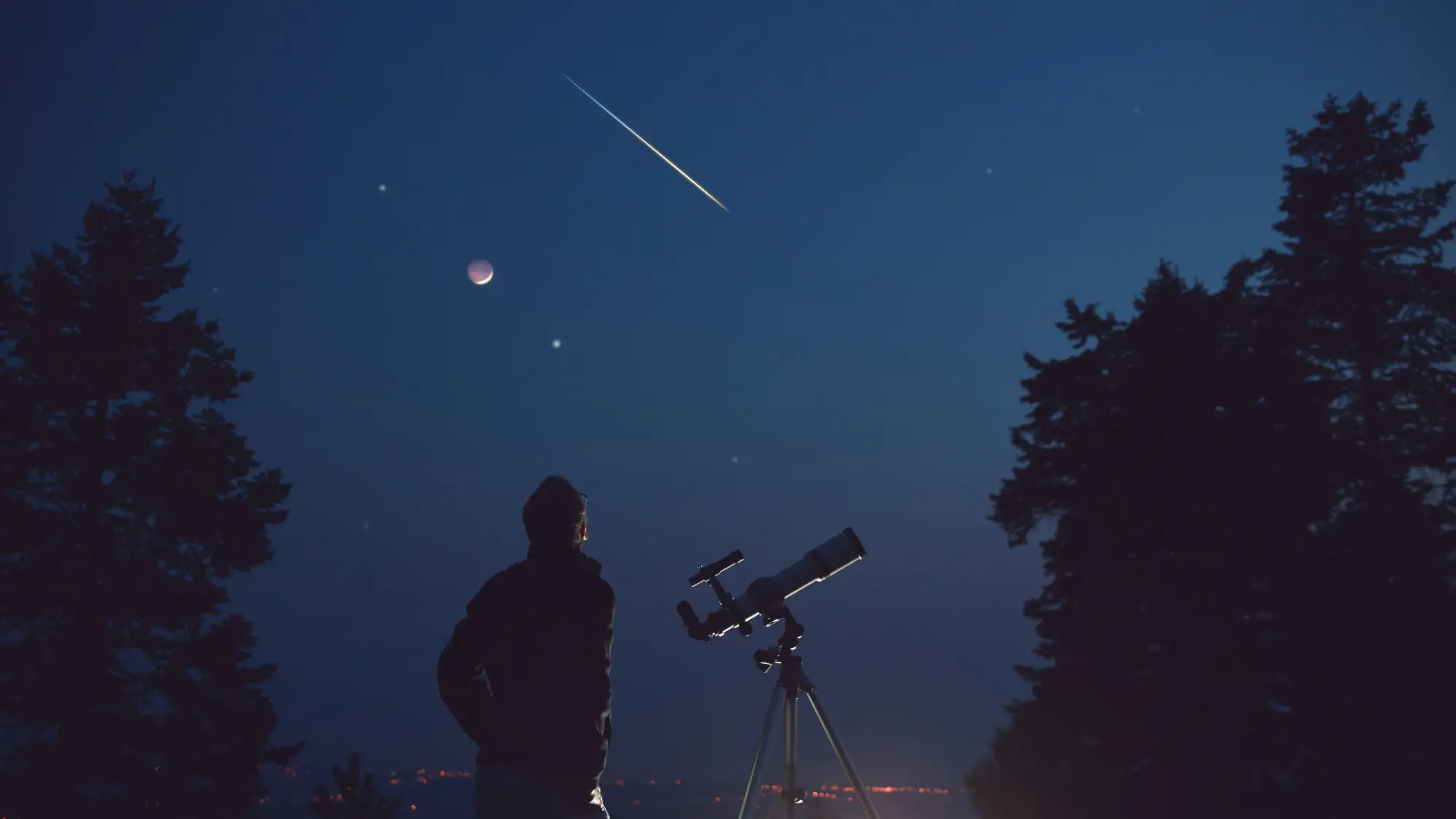 Muž s teleskopem pozorující večerní oblohu
