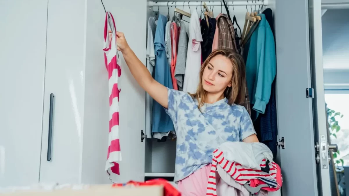 Žena přemýšlí nad výběrem oblečení před otevřenou šatní skříní.