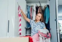 Žena přemýšlí nad výběrem oblečení před otevřenou šatní skříní.