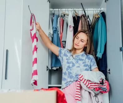 Žena přemýšlí nad výběrem oblečení před otevřenou šatní skříní.
