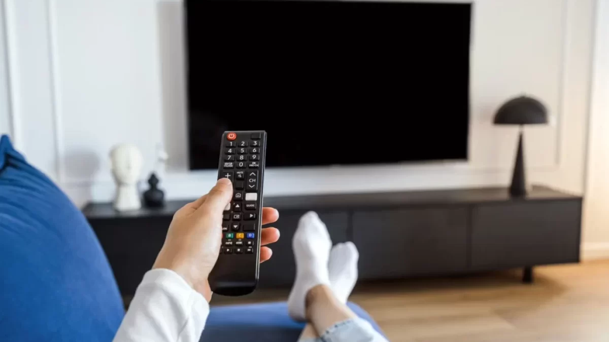 Muž na gauči drží ovladač namířený na televizi