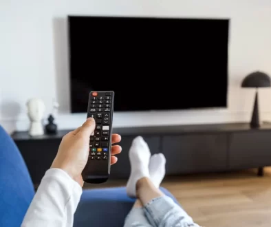 Muž na gauči drží ovladač namířený na televizi