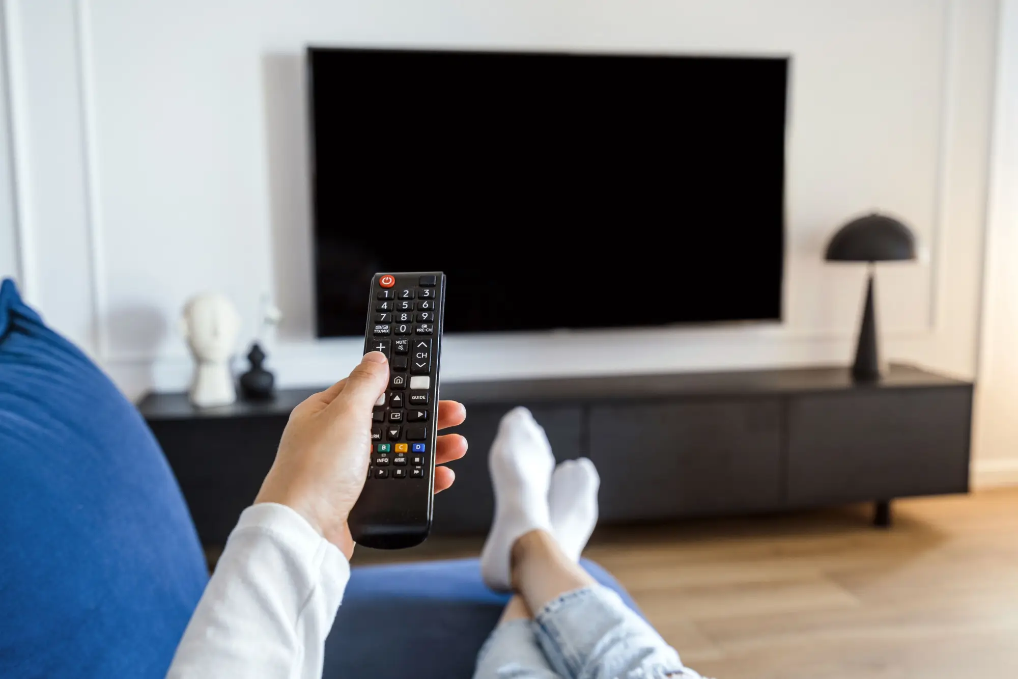 Muž na gauči drží ovladač namířený na televizi