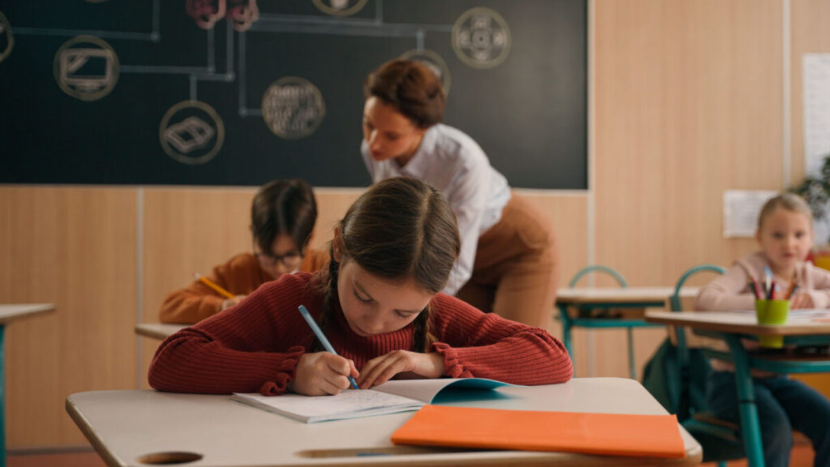 žákyně sedící ve třídě u stolu si dělá zápisky