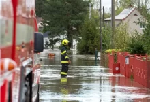 Hasič stojí ve vodě na zaplavené ulici mezi domy.