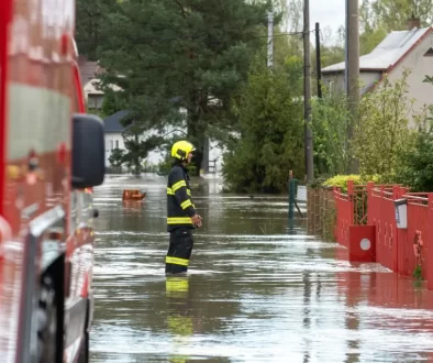 Hasič stojí ve vodě na zaplavené ulici mezi domy.