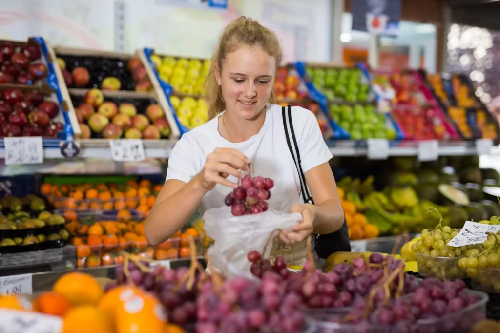 Žena vybírá červené hrozny v oddělení čerstvého ovoce v supermarketu.