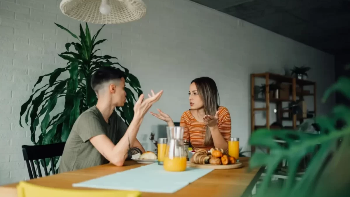 Napjatá atmosféra mezi mužem a ženou v moderní kuchyni, sedí u stolu obklopeni pokojovými rostlinami.