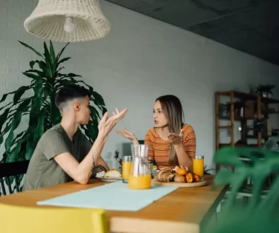Napjatá atmosféra mezi mužem a ženou v moderní kuchyni, sedí u stolu obklopeni pokojovými rostlinami.