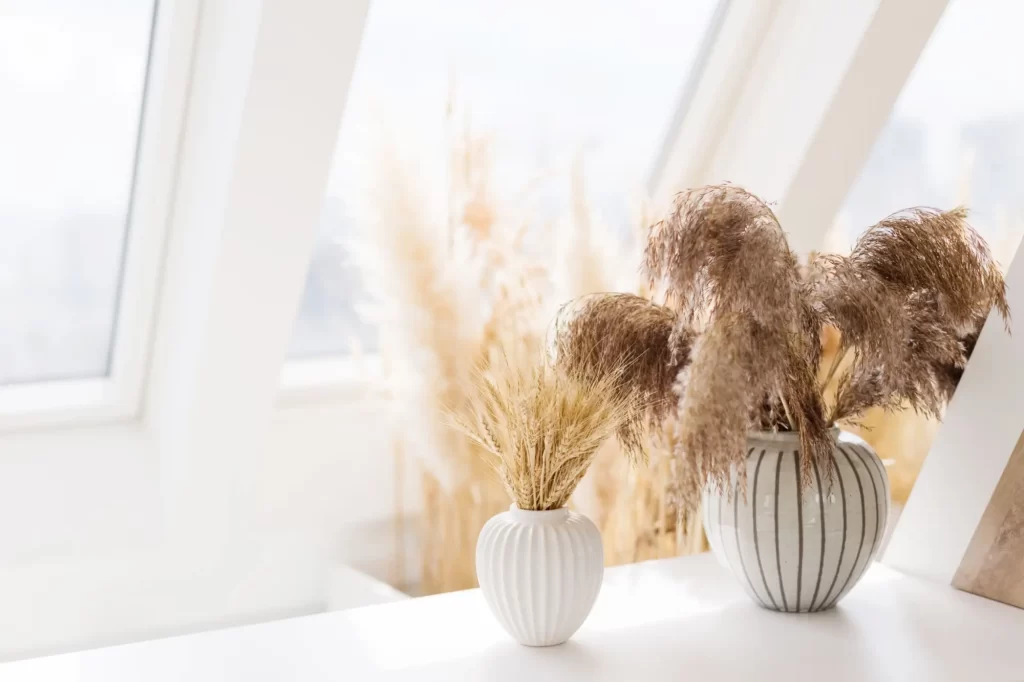Detail sušené pampové trávy ve dvou designových vázách na parapetu moderního interiéru.