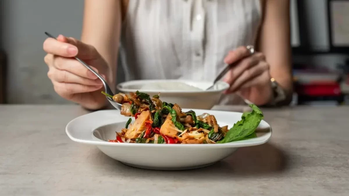 Mladá žena sedí za stolem, v ruce drží příbor a chystá se jíst krásně barevné veganské jídlo