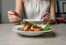 Mladá žena sedí za stolem, v ruce drží příbor a chystá se jíst krásně barevné veganské jídlo