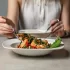 Mladá žena sedí za stolem, v ruce drží příbor a chystá se jíst krásně barevné veganské jídlo