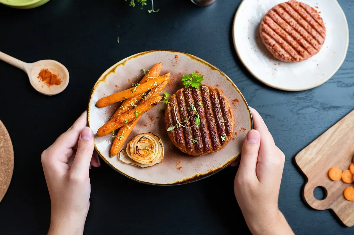 Vegan 3 - SportDeník Pestrý talíř se zeleninou a náhražkou masa a ruce, které ho drží