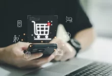 Muž sedící u počítače drží v ruce telefon, nad ním je virtuální ikonka košíku s dvěma položkami