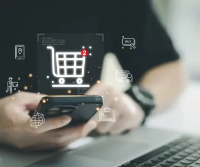 Muž sedící u počítače drží v ruce telefon, nad ním je virtuální ikonka košíku s dvěma položkami