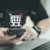 Muž sedící u počítače drží v ruce telefon, nad ním je virtuální ikonka košíku s dvěma položkami