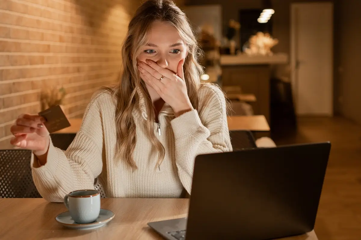 Mladá vyděšená žena sleduje s rukou přes ústa pohyb peněz na svém účtu přes online aplikaci