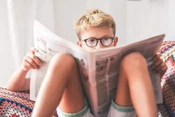 Asi desetiletý blonďatý chlapec sedí na sedačce a půl obličeje mu zakrývá časopis