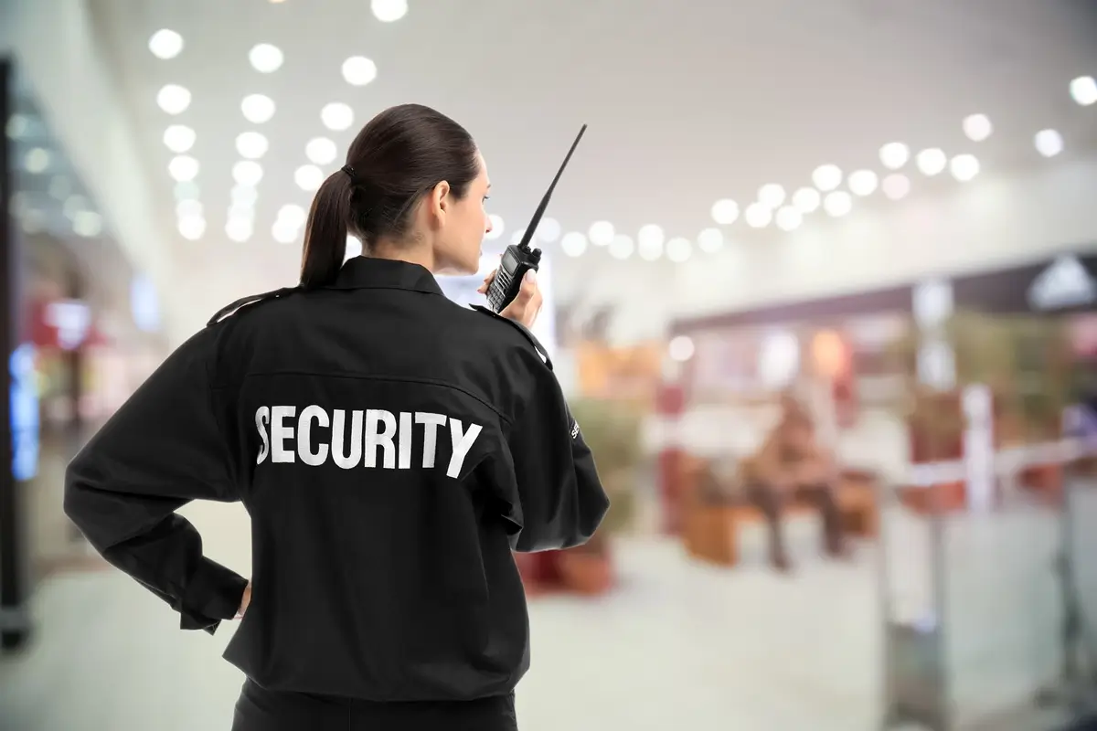 Pracovnice security stojí v supermarketu a mluví do vysílačky