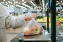 Ruka vkládající sáček s jablky na váhu samoobslužné pokladny