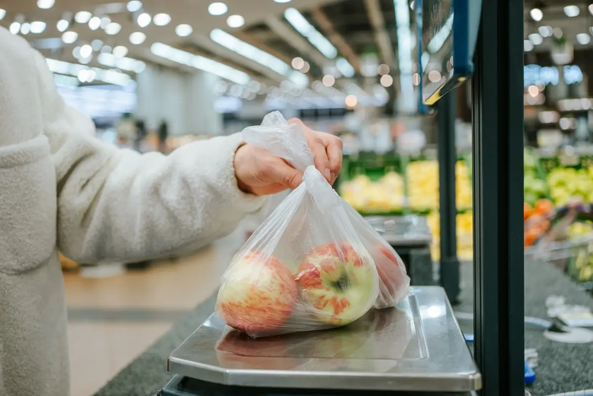 Ruka vkládající sáček s jablky na váhu samoobslužné pokladny