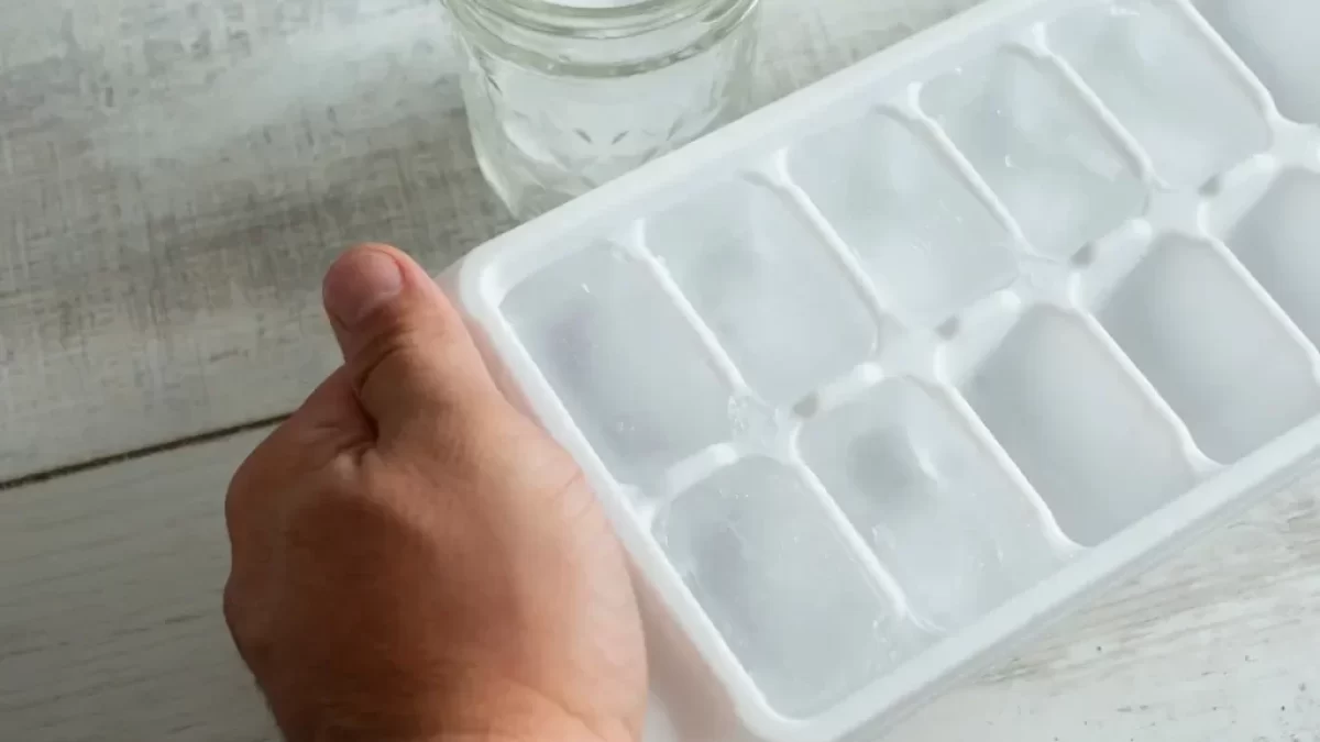 Plato s kostkami ledu a mužská ruka, která jej drží