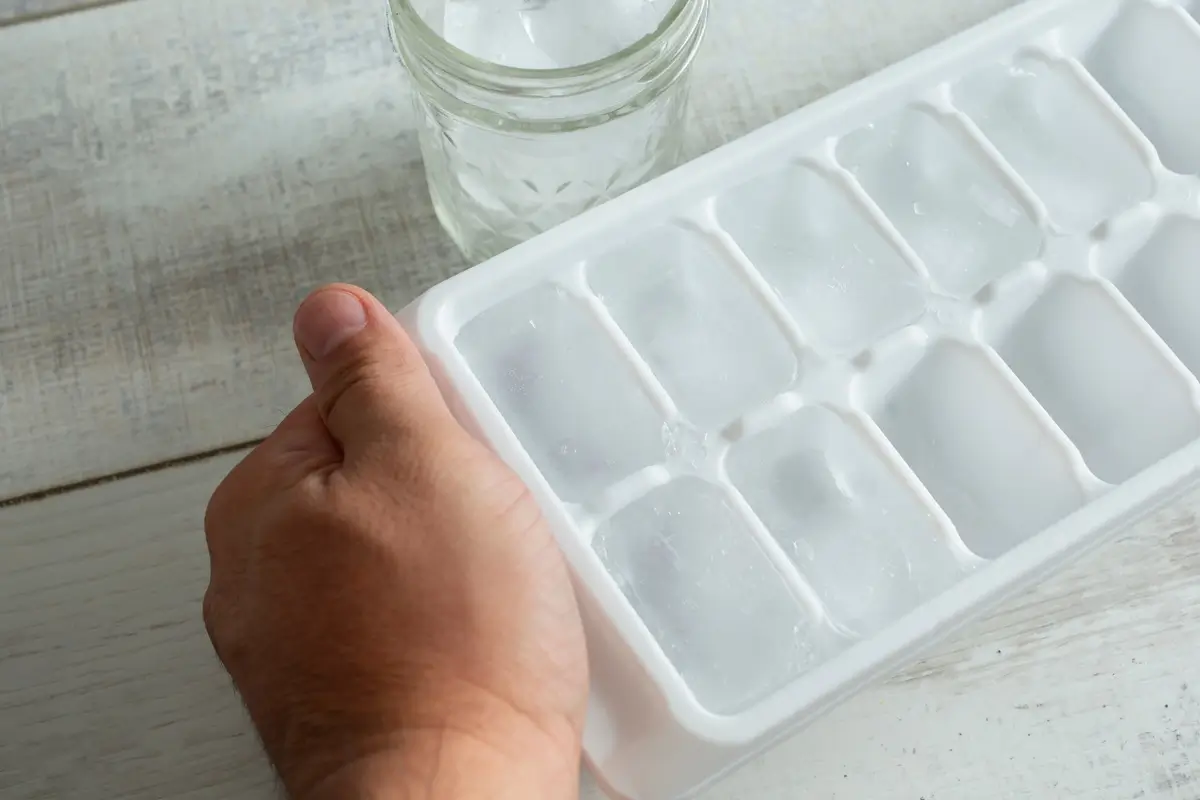 Plato s kostkami ledu a mužská ruka, která jej drží