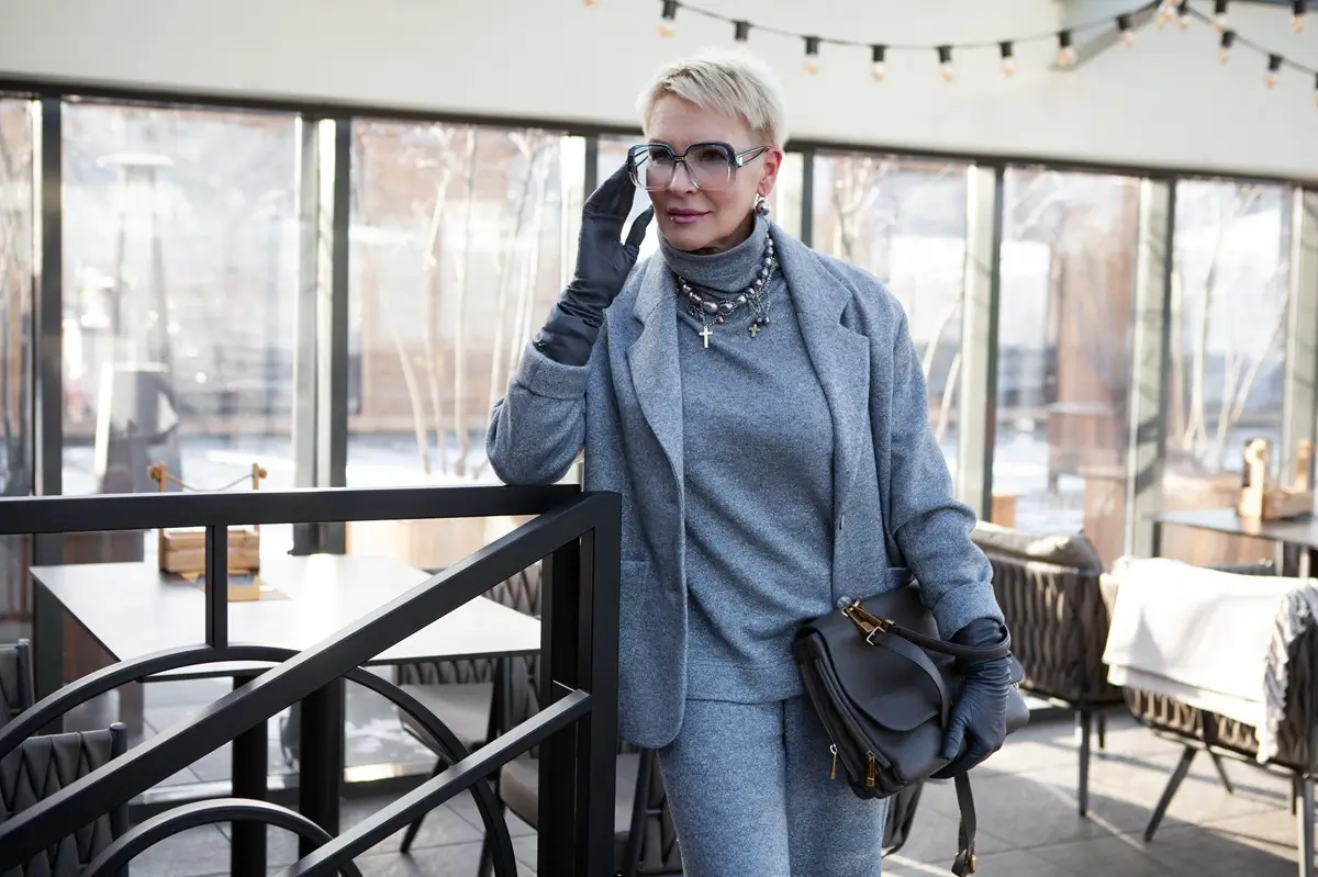 Dáma 60+ v elegantním modrém kostýmu s rolákem a slunečními brýlemi