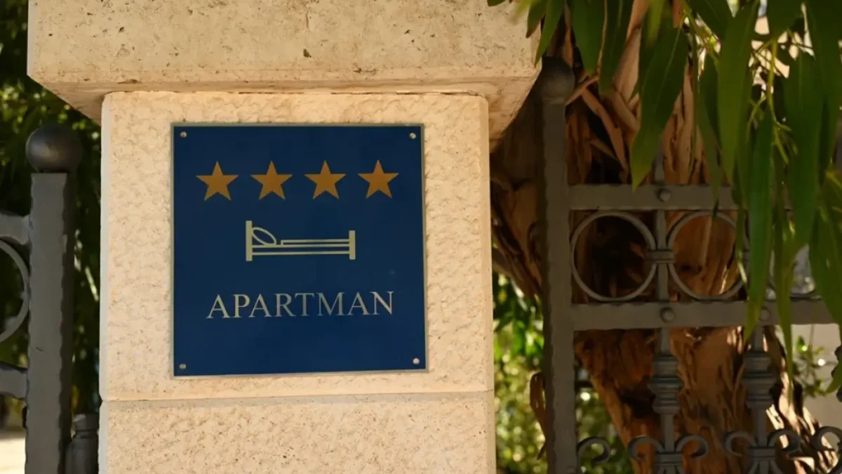 Sloupek domu s cedulkou, na které je napsáno "Apartmani"