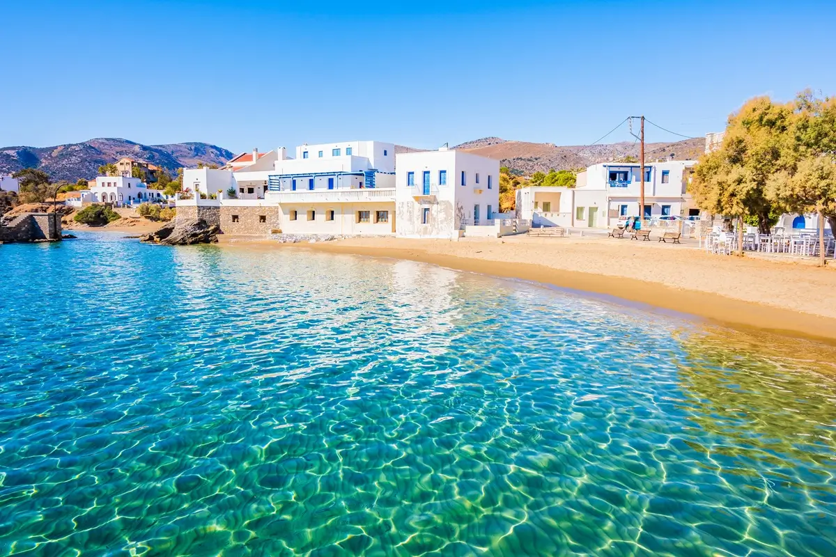 Průzračně křišťálové moře a v pozadí nízké domy s apartmány na ostrově Naxos