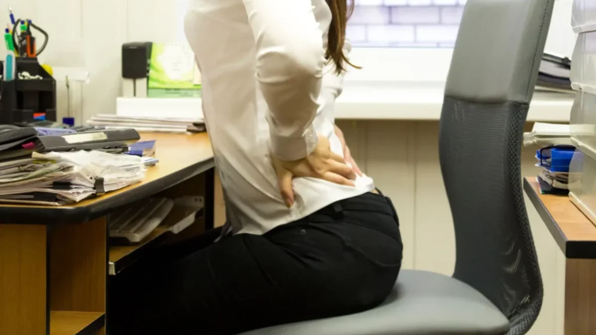 žena sedící v kanceláři u stolu se drží za bolavá bedra