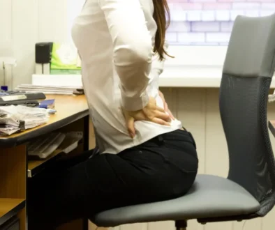 žena sedící v kanceláři u stolu se drží za bolavá bedra