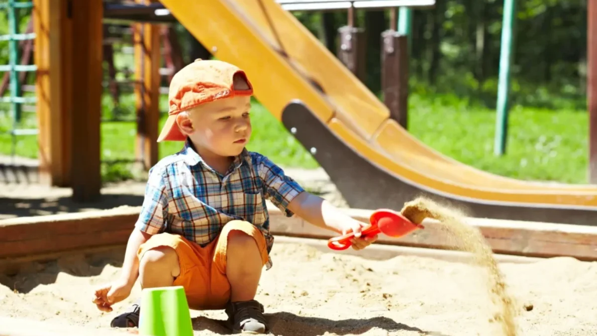 Malý chlapec si hraje s hračkami v pískovišti na dětském hřišti.
