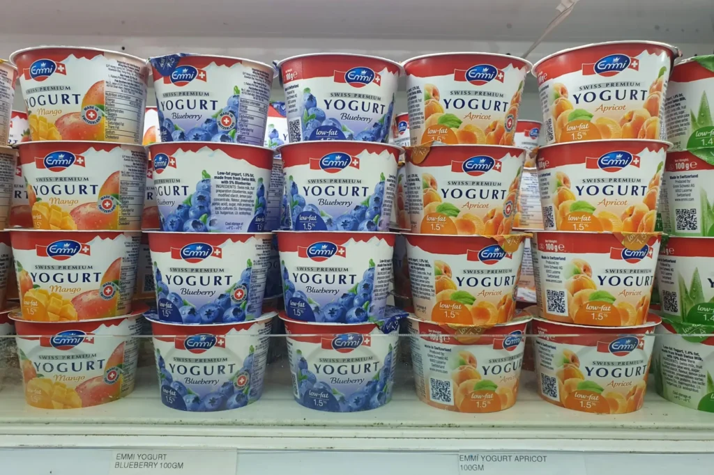 Barevné kelímky ochucených jogurtů vystavené v chladicím regálu supermarketu.