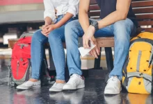 Dva cestovatelé s batohy sedí na lavičce na nádraží.