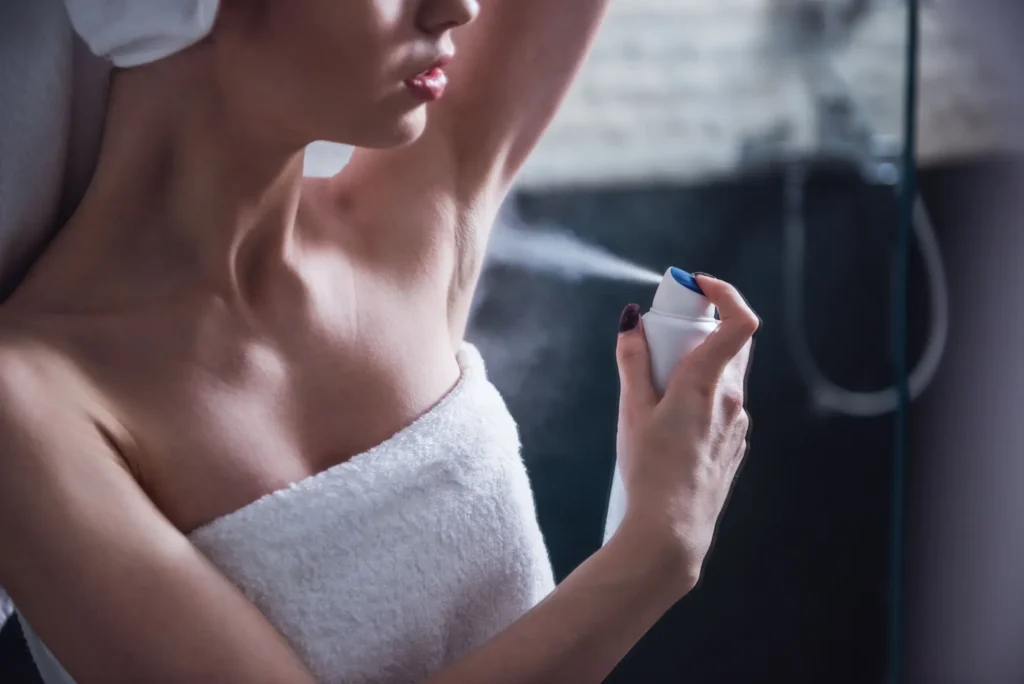 Shutterstock_2367546207 - SportDeník Žena ve sprše v ručníku si aplikuje deodorant do podpaží