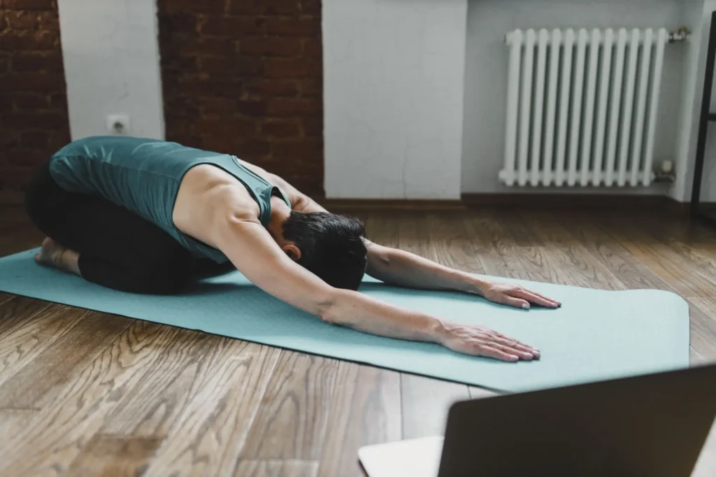- SportDeník Žena cvičí pozici dítěte (Balasana) na podložce v interiéru.
