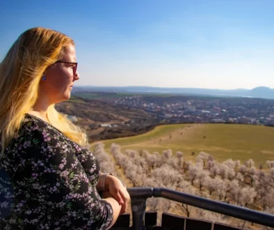 Žena stojící na vyhlídce a dívající se do dálky na krajinu.