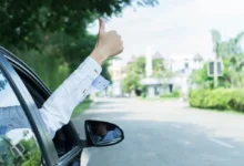 Záběr na přední část vozu, z kterého je vystrčená mužská ruka, ukazující palcem "jedničku"