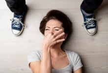 Mladá žena leží na zemi a drží si nos, vedle ní jsou mužské nohy v teniskách